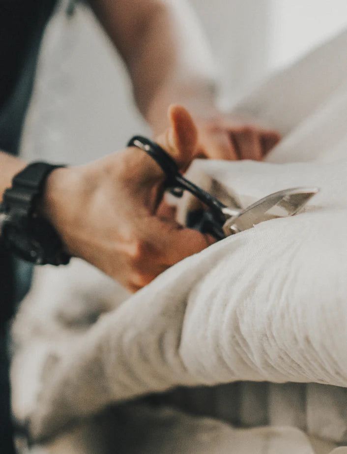 hand wearing a watch, using scissors to cut a piece of material